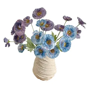 Fleurs de pavot bleues artificielles dans un vase en céramique beige texturé