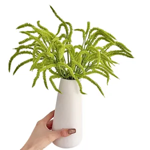 Artificial drooping green plant in a white ceramic vase held by hand for home decor