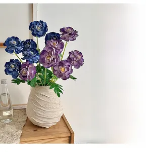 Detailed view of artificial blue and purple peonies in a textured beige ceramic vase