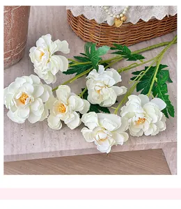 Detail view of realistic white artificial peonies with green leaves on marble surface
