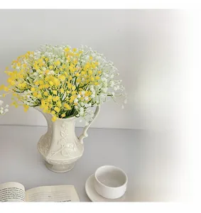 Artificial babys breath flowers in ceramic vase on desk with book and coffee cup decor