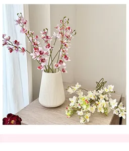 Pink and white artificial orchid bouquet in a white textured ceramic vase on a wooden table