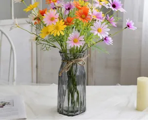 Detalle del jarrón de vidrio gris a rayas con margaritas de seda de colores y un lazo