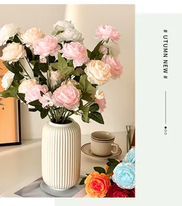 Close-up of colorful faux silk peonies in a white ceramic vase with a warm home setting