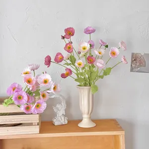 Silk poppy flowers in various colors arranged in a cream ribbed vase on a wooden tray
