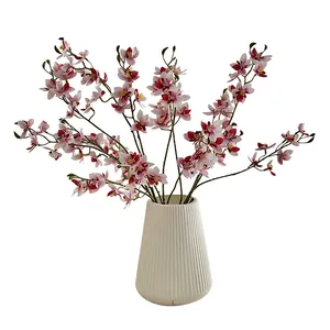 Artificial white orchid flowers with pink centers in a textured white ceramic vase