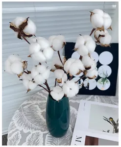 Top view of natural cotton flower arrangement in a dark green ceramic vase on a tablecloth