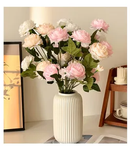 Close-up of artificial pink and white peonies with green leaves in a home decor setting