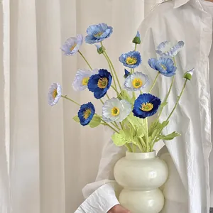 Elegant artificial corn poppy arrangement in white ceramic vase held by a model