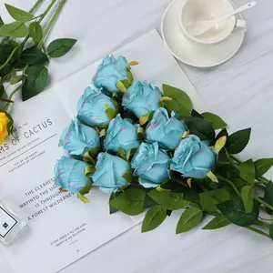 Detail of 11 artificial blue roses with silk petals and green leaves on marble surface