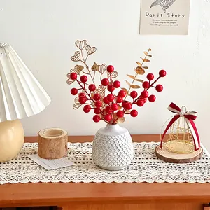 Artificial red berries and golden leaves in white textured ceramic vase for home decor