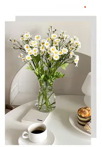 Artificial white daisy bouquet in a glass vase with coffee and dessert on a table