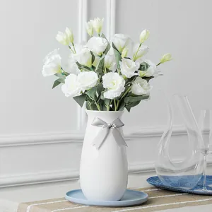 Elegant white artificial Eustoma flowers in a ceramic vase with a grey ribbon bow