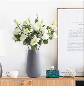 White faux Eustoma flowers in a textured grey ceramic vase on a wooden cabinet
