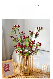 Close-up of faux red pomegranate berry branches in a gold frame glass vase on bamboo table