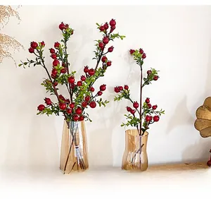 Close-up of artificial pomegranate branch with red berries in an amber glass vase