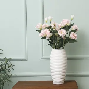 Pink artificial Lisianthus flowers in a white wave textured vase on a wooden shelf