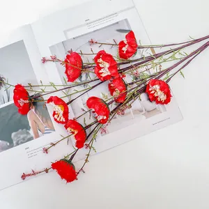 Close-up of artificial red silk flowers with green leaves and pink berries on white desk