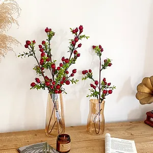 Artificial red pomegranate berry branches in amber glass vases for home decor