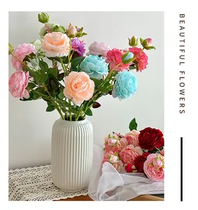 Detailed arrangement of colorful artificial peonies in a white ceramic vase on a lace tablecloth