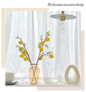 Vibrant artificial lemon branches in an amber glass vase with white sheer curtains