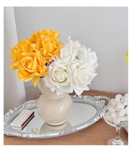Detail of lifelike silk roses in a ceramic vase on an elegant mirrored silver tray