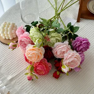 Vibrant mixed silk peony bouquet with green leaves on white textured tablecloth