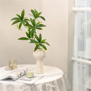 Detailed view of white ceramic gourd vase with faux greenery on a lace tablecloth