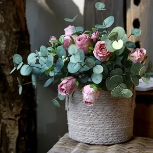 Rosa Kunstrosen mit Eukalyptusblättern in einem grauen geflochtenen Korb Blumenarrangement