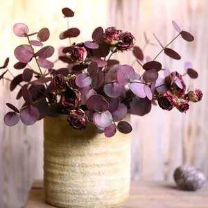 Detail von künstlichen Eukalyptusblättern und roten Trockenrosen in gerippter Vase