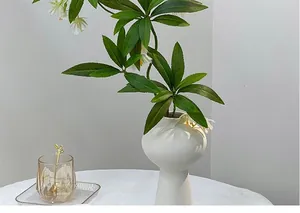 Macro detail of white ceramic vase with spiral texture and artificial green plant leaves