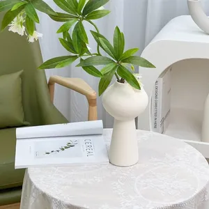 Minimalist white ceramic vase with green foliage plant in a modern home decor setting