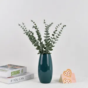 Branches d'eucalyptus artificiel dans un vase en céramique vert foncé sur nappe blanche
