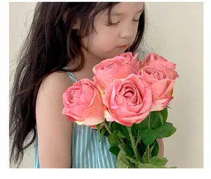 Close-up of pink artificial roses with realistic petals and green leaves held by a girl