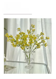 Macro detail of yellow artificial flowers in a ribbed glass vase near white curtains