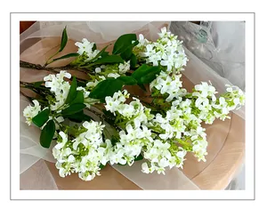 Close-up of white silk lilac petals and green leaves on a realistic brown branch