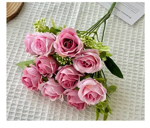 Close-up of artificial 10-head pink silk roses with green leaves on white texture