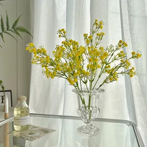 Artificial yellow baby breath flowers in a relief glass vase on a reflective desk