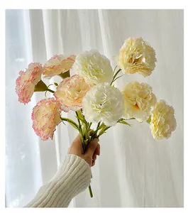 Detail of faux silk carnations in cream and pink tones held against soft white curtains