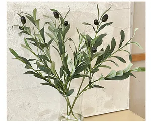 Close-up of lifelike artificial olive branches with green leaves and black fruits in glass vase
