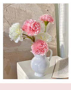 Close-up of artificial pink and white carnations in a minimalist white ceramic vase
