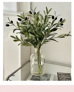 Detail of artificial olive branch with dark fruits in a clear glass vase on a table