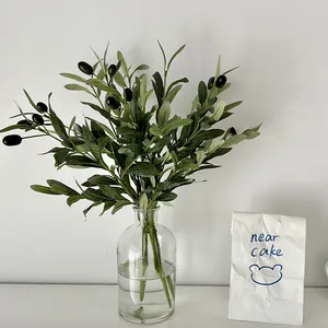 Artificial olive branch with green leaves and black fruits in a glass vase decor