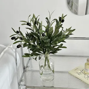 Realistic artificial olive branches with purple fruits in a sleek glass vase on a trolley