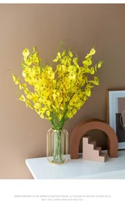 Detail of yellow artificial dancing orchids in glass vase with golden metal frame stand