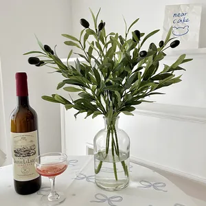 Artificial olive branches with green leaves and fruits in a glass vase for home decor