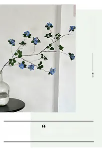 Artificial branch with blue flowers in a glass vase against a white minimalist wall