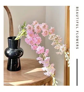 Pink artificial cherry blossom flowers in a black geometric ceramic vase on a wooden table