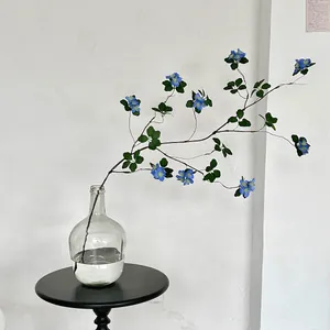Minimalist blue artificial apricot flower in a clear glass vase on a black table
