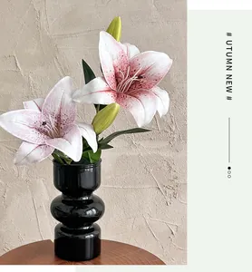 Close-up of pink 3D artificial lilies in a tiered black ceramic ring vase on wooden table